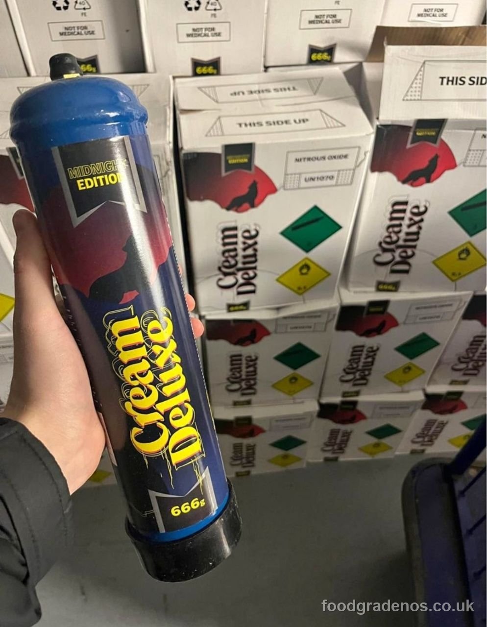 A hand holding a Cream Deluxe Midnight Edition food-grade nitrous oxide cylinder